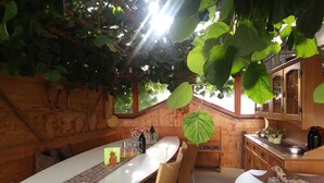 A rustic wooden cabin with a dining area featuring a long table, wicker chairs, and a hanging leaf decoration. - Farm with small animals, petting zoo, trial riding, beautifully situated. (Tarsch)
