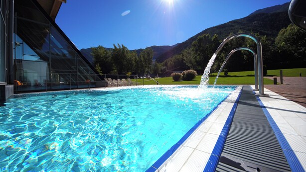 A swimming pool with clear blue water, a metal handrail, and a view of mountains in the background. - Farm with small animals, petting zoo, trial riding, beautifully situated. (Tarsch)