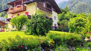 A two-story chalet with balconies, surrounded by a well-maintained garden with various flowers and shrubs. - Farm with small animals, petting zoo, trial riding, beautifully situated. (Tarsch)