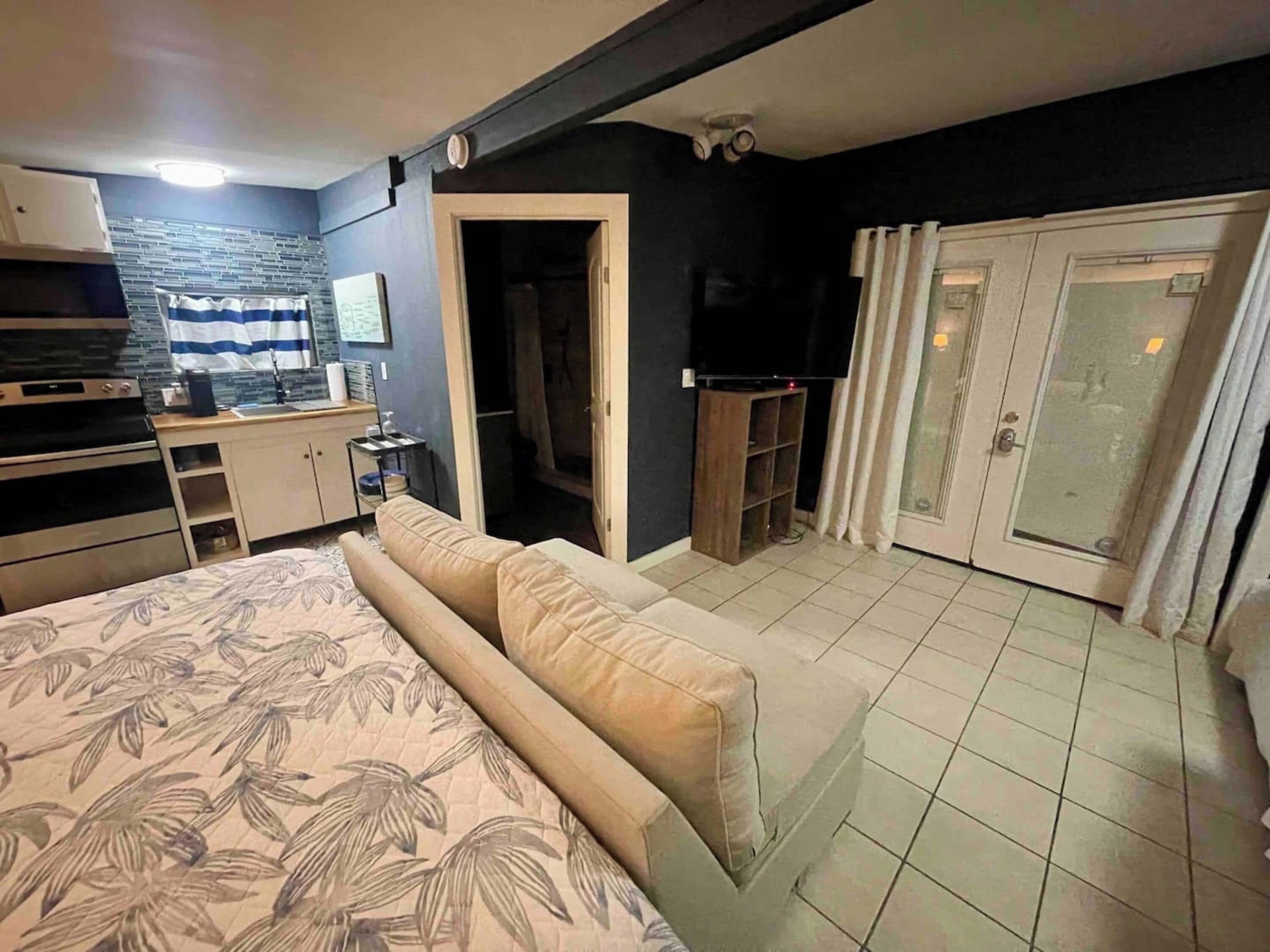 Un dormitorio con cama, televisor, kitchenette y baño.