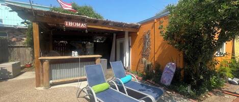 An outdoor seating area with two lounge chairs and a bar named 'THOMAS'.