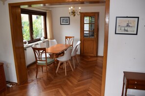 Un comedor con mesa y sillas de madera, una araña y obras de arte en las paredes.