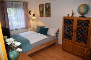 Ein Schlafzimmer mit einem Bett, einem Holzkabinett mit Glastüren, einem Globus und zwei gerahmten Bildern an der Wand.