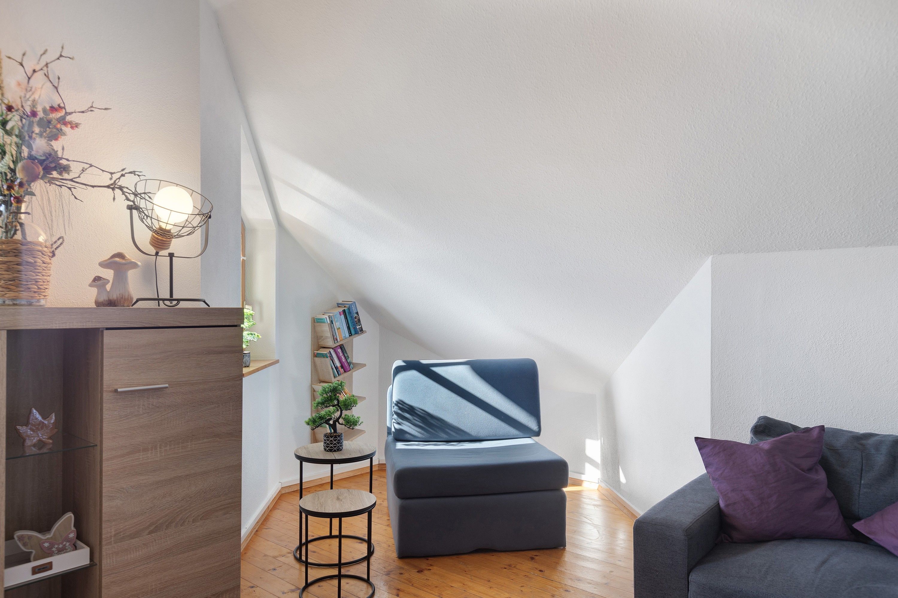 Ein modernes Wohnzimmer mit einem grauen Sofa, einem kleinen runden Tisch und einem Bücherregal.