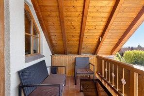 Un balcon en bois doté d’un plafond incliné, d’une fenêtre et de deux chaises.