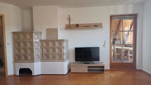 Un salon équipé d’un téléviseur, de meubles en bois, d’une cheminée et d’un coin repas visible à travers une porte vitrée.