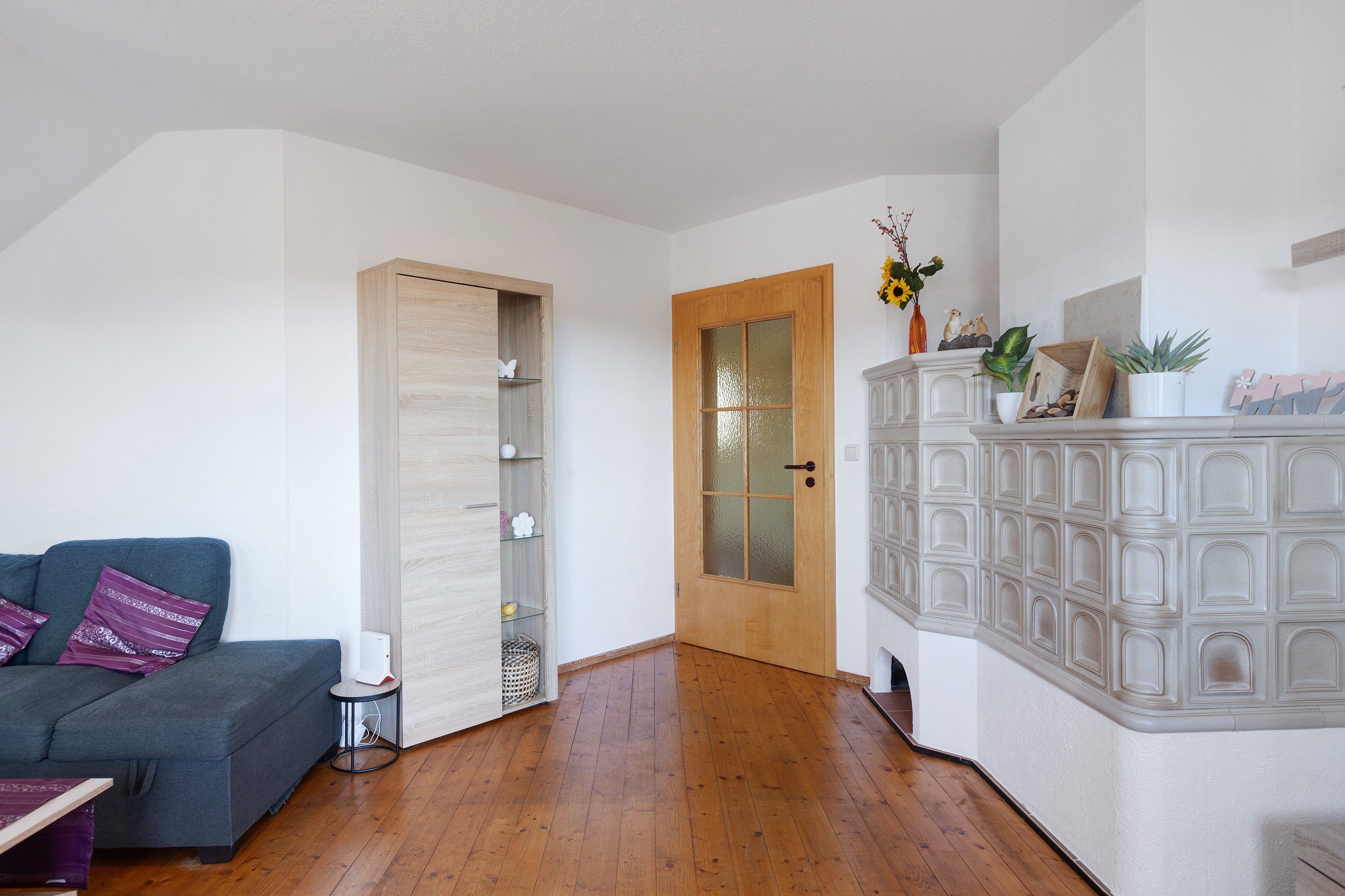 A room with a grey sofa, a wooden cabinet with glass doors, and a wooden floor.