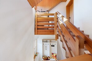 Un escalier en bois avec une rampe, menant à un palier doté d’un mur blanc et d’une fenêtre.
