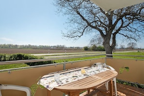 Ein Balkon mit Tisch, Stühlen und Blick auf Felder und Bäume.