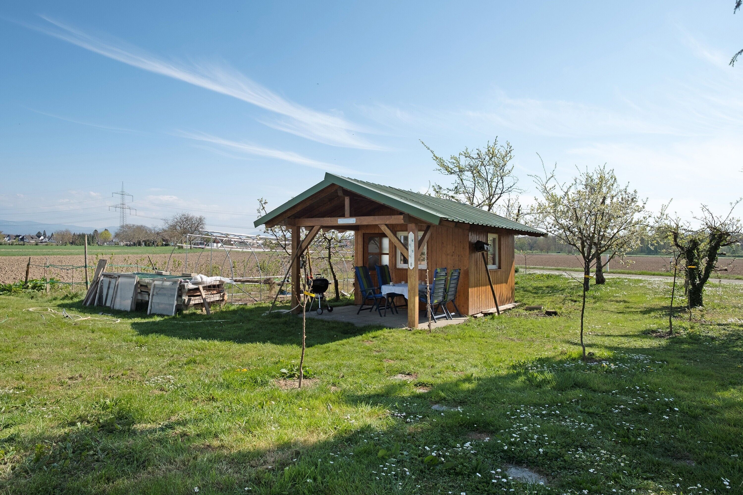 Eine Holzhütte mit einem grünen Dach, einem Tisch, Stühlen und einem kleinen Garten.