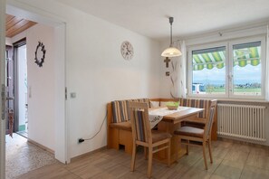 Een eetgedeelte met een houten tafel, stoelen, een bank, een wandklok en een raam met uitzicht.