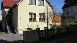 A two-story building with a sloped roof, a staircase leading to the entrance, and a paved driveway. - Auenweg Apartment with Shared Pool, Garden, and Wi-Fi (Radebeul)