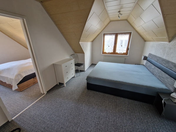 A bedroom with a sloped ceiling, a bed, a dresser, a chair, and a window.