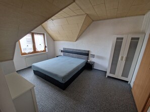 Une chambre à coucher avec un lit, une armoire, une table de chevet, une lampe et une fenêtre.