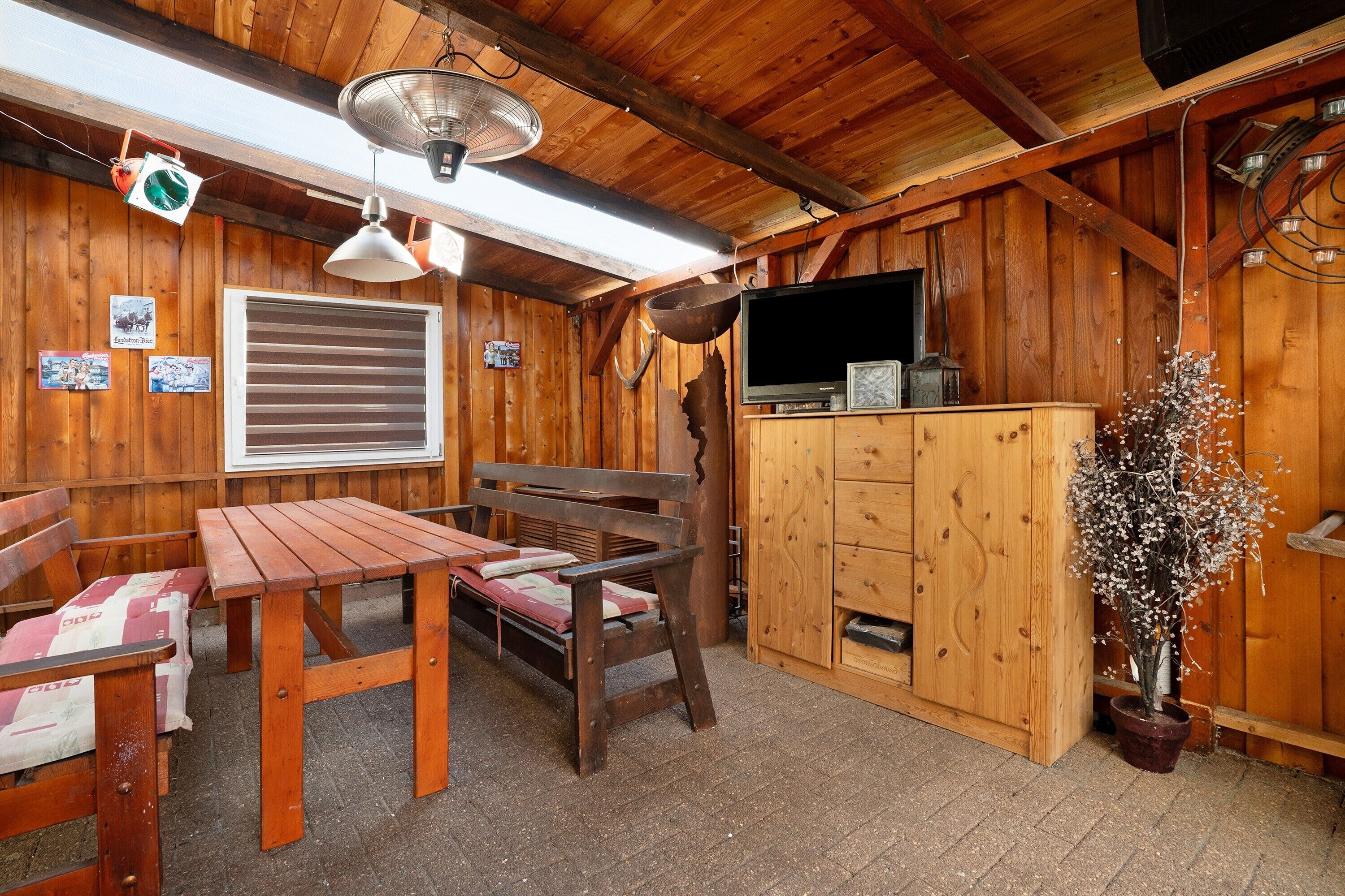 A wooden interior with a table and benches, a fan, a television, and a potted plant.