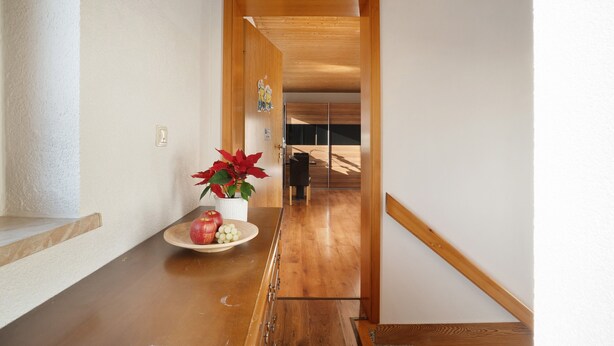 Un pasillo con suelo de madera, pared blanca y una puerta que da a otra habitación.