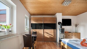 Un dormitorio moderno con techo de madera, una cama con colcha azul, un televisor montado en la pared y un armario de madera.