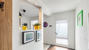 Um corredor com porta de madeira, planta amarela, quadros emoldurados e um sinal roxo circular.