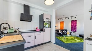 Cozinha moderna com pia, bancada e armários. Há uma área de refeições com sofá e mesa de centro.