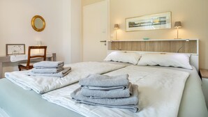 Une chambre d’hôtel comprenant un lit, deux tables de chevet, une chaise, un miroir, un tableau encadré et une peinture au mur.