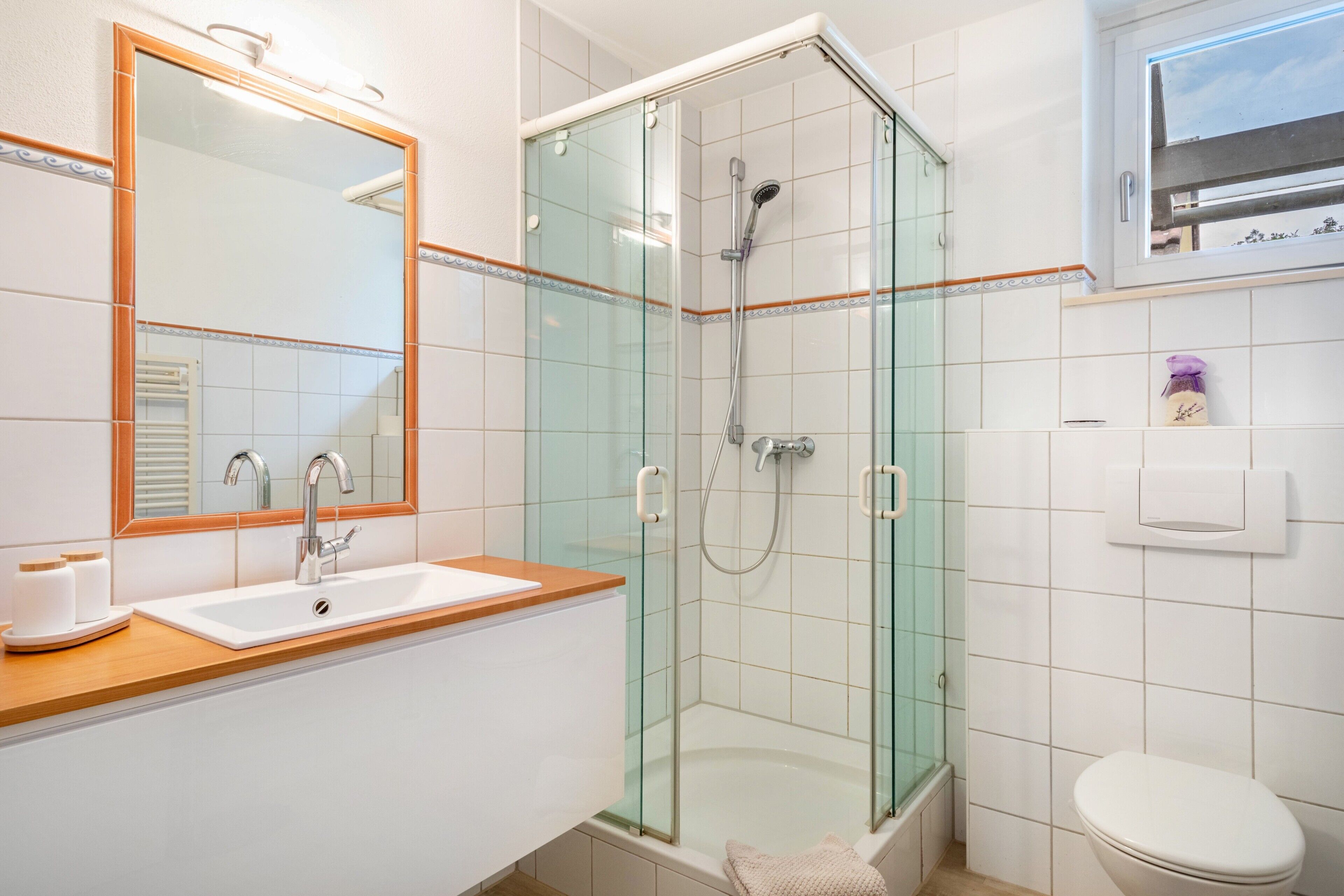 Een badkamer met een douchecabine van glas, een wastafel met spiegel en een toilet.