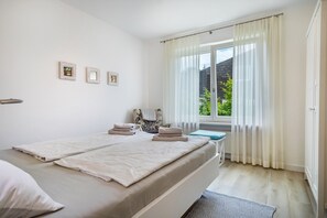 A bedroom with a bed, a small table, a chair, and a window with curtains.