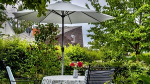 Une terrasse avec une table et des chaises, un parasol blanc et un vase rempli de fleurs.