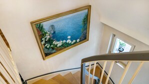 Un escalier en bois avec une rampe, un tableau représentant un paysage côtier et une fenêtre donnant sur l’extérieur.