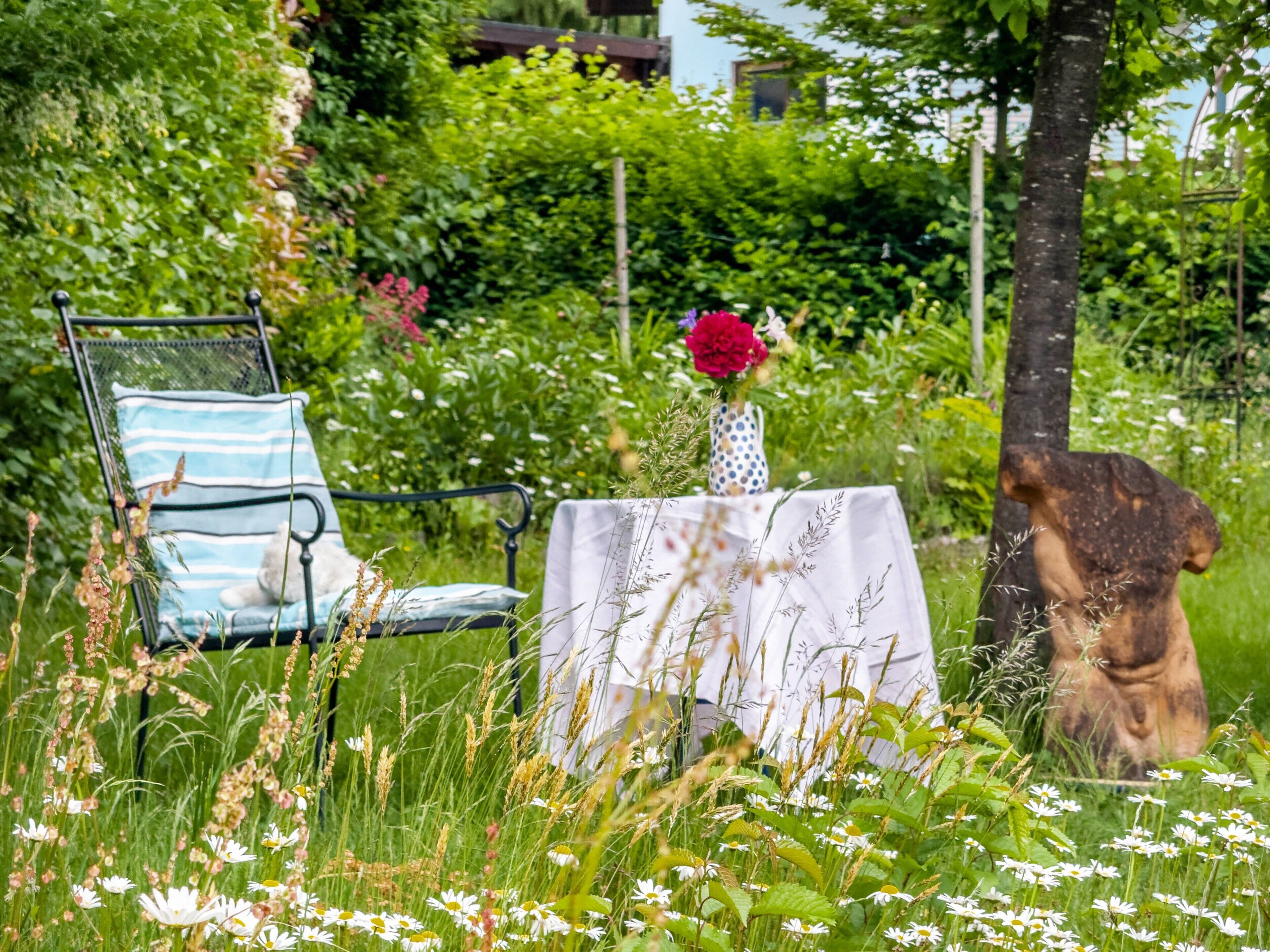A garden setting with a table, a chair, and a vase of flowers.