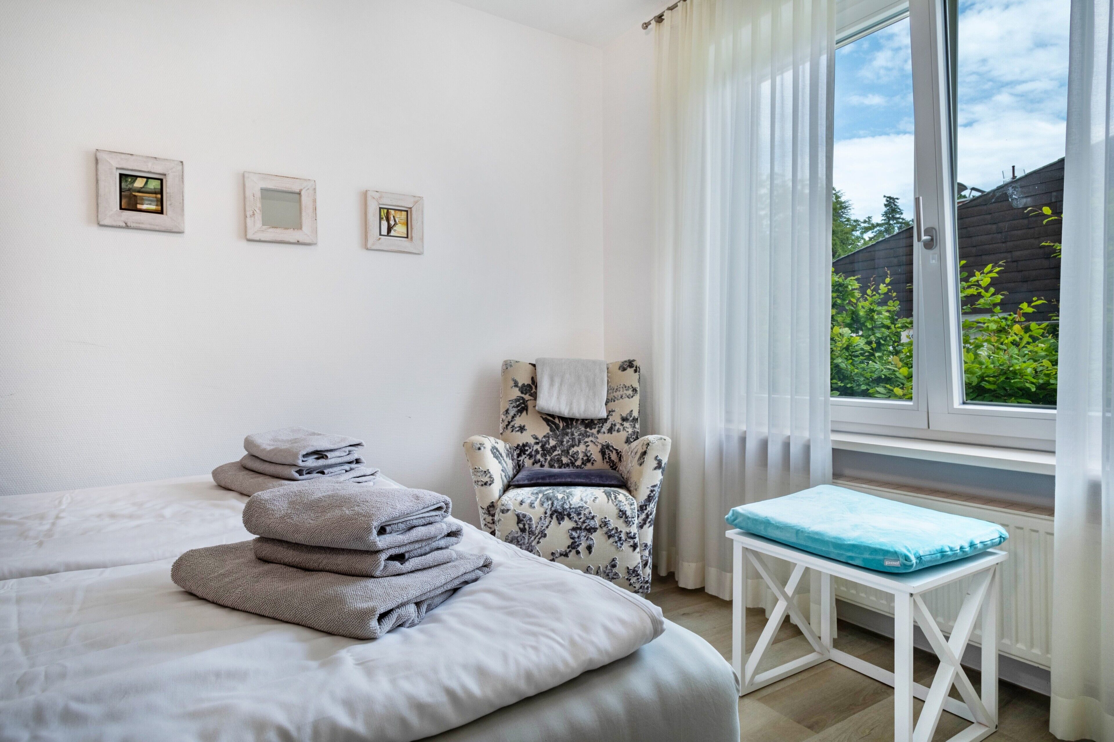 Een slaapkamer met een bed, een stoel, een klein tafeltje en een raam met uitzicht op groen.