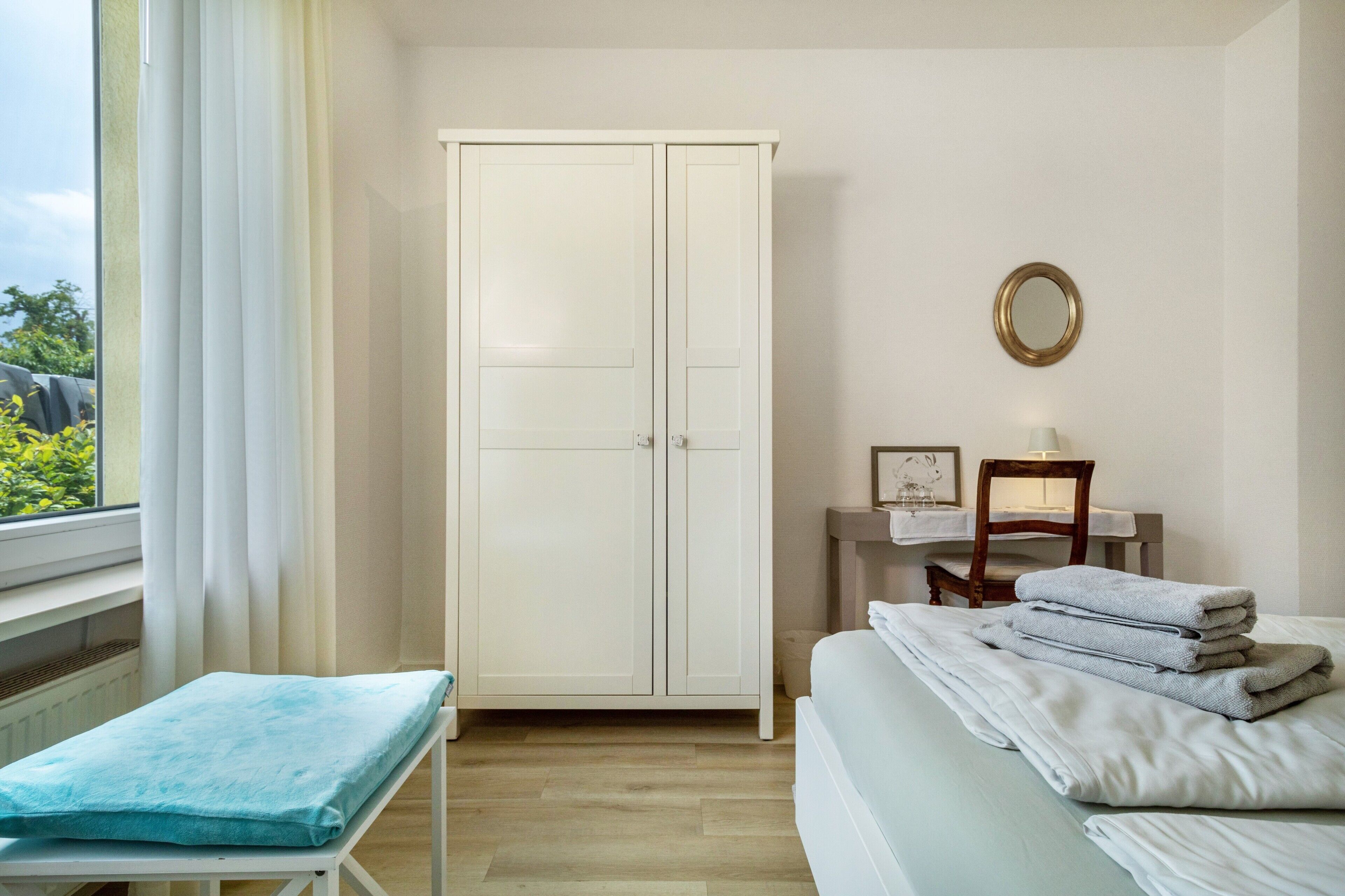 Quarto com cama, mesa de cabeceira, cadeira, guarda-roupa e janela com cortinas.