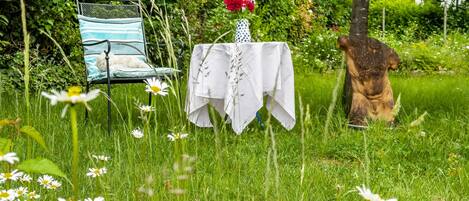 A garden with a chair, a table with a white cloth, and a statue.