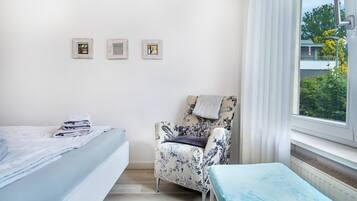 Un dormitorio con una cama, una silla y una ventana con vistas a zonas verdes.