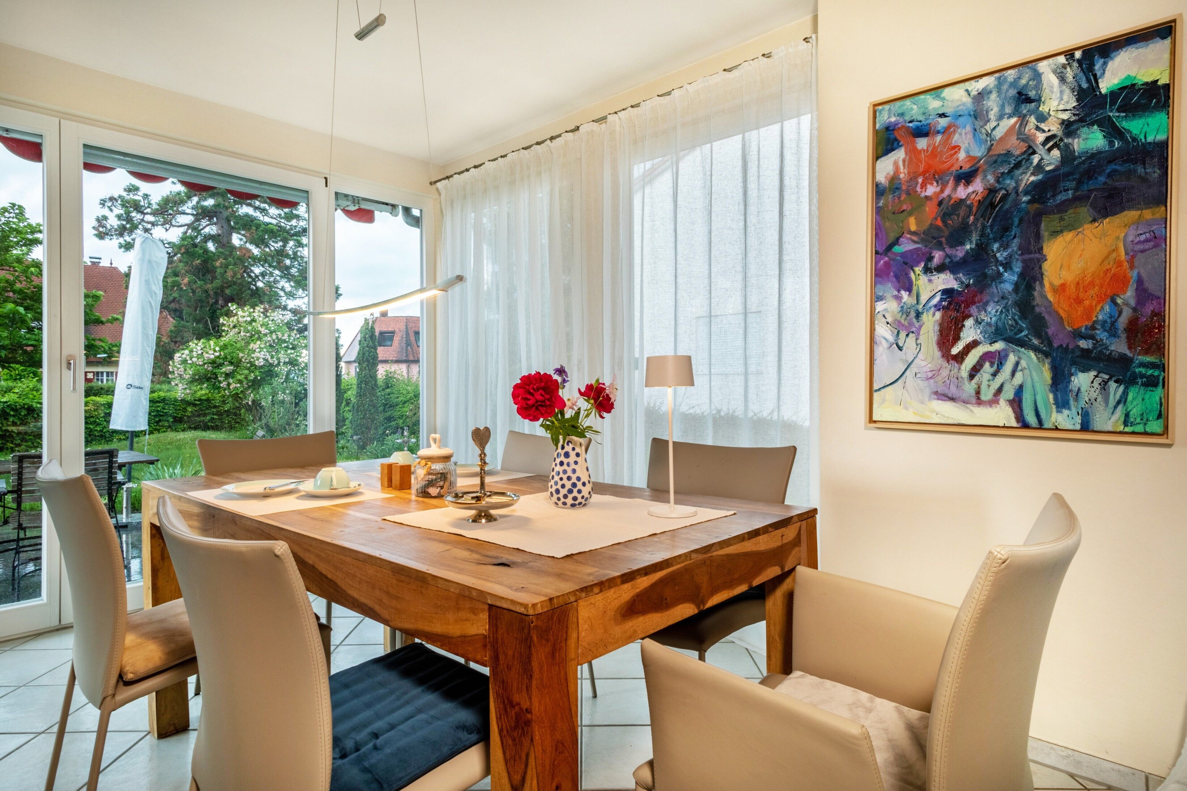 Un comedor con una mesa de madera, sillas, un florero con flores y un cuadro en la pared.