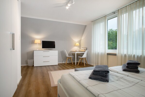 Una habitación de hotel moderna con una cama, un escritorio, una silla, un televisor y una ventana con cortinas.