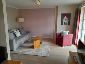 A modern living room with a grey sofa, a red armchair, a small wooden coffee table, and a patterned rug. - Apartment 'Am Kniebach' with Balcony and Wi-Fi (Immenstaad am Bodensee)