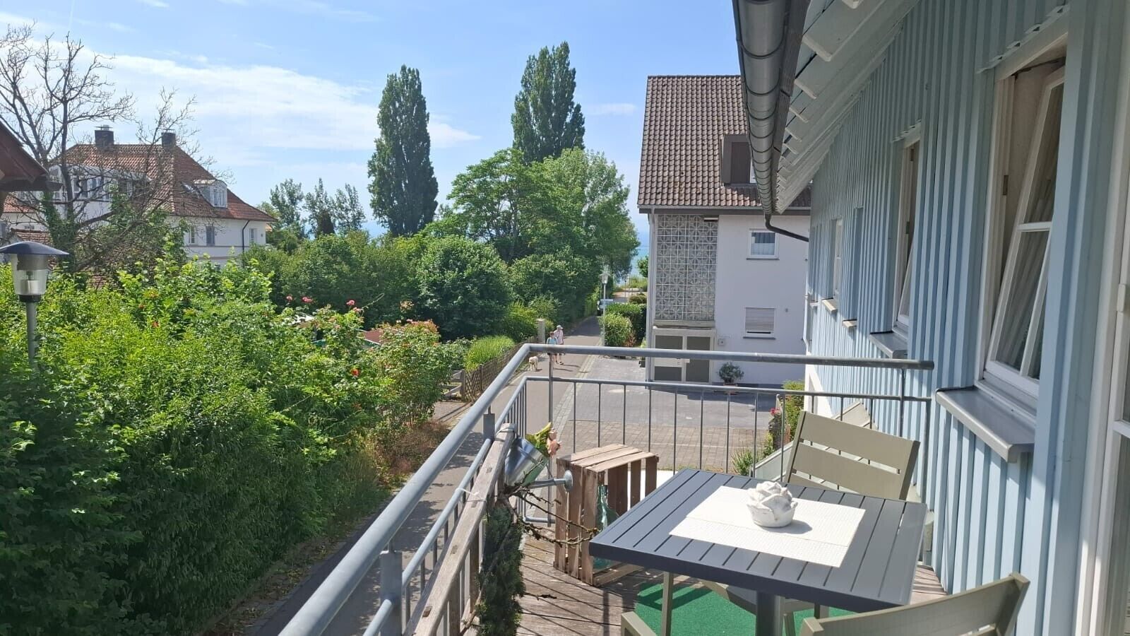 Un balcone con tavolo e sedie, vista su un giardino e una strada.