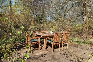 Un ensemble de table et de chaises en bois, installé dans un jardin où le feuillage est luxuriant et où l’on aperçoit des arbres en arrière-plan.