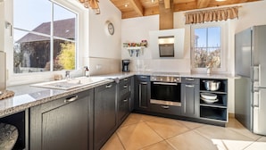 A modern kitchen with dark cabinets, a stainless steel oven, and a large window. - Geyerbad Holiday Home with Private Sauna – Dream Vacation High on the Swabian Alps (Meßstetten)
