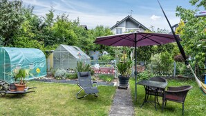 Un patio jardín con mesa y sillas, un invernadero y una zona de estar cubierta.
