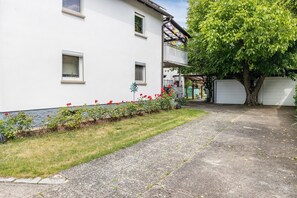 A white building with a paved driveway, a tree, and a small garden with red flowers. - Apartment 'A Casa Alfred Kemmern - Neu' with Shared Terrace, Wi-Fi and Air Conditioning (Kemmern)