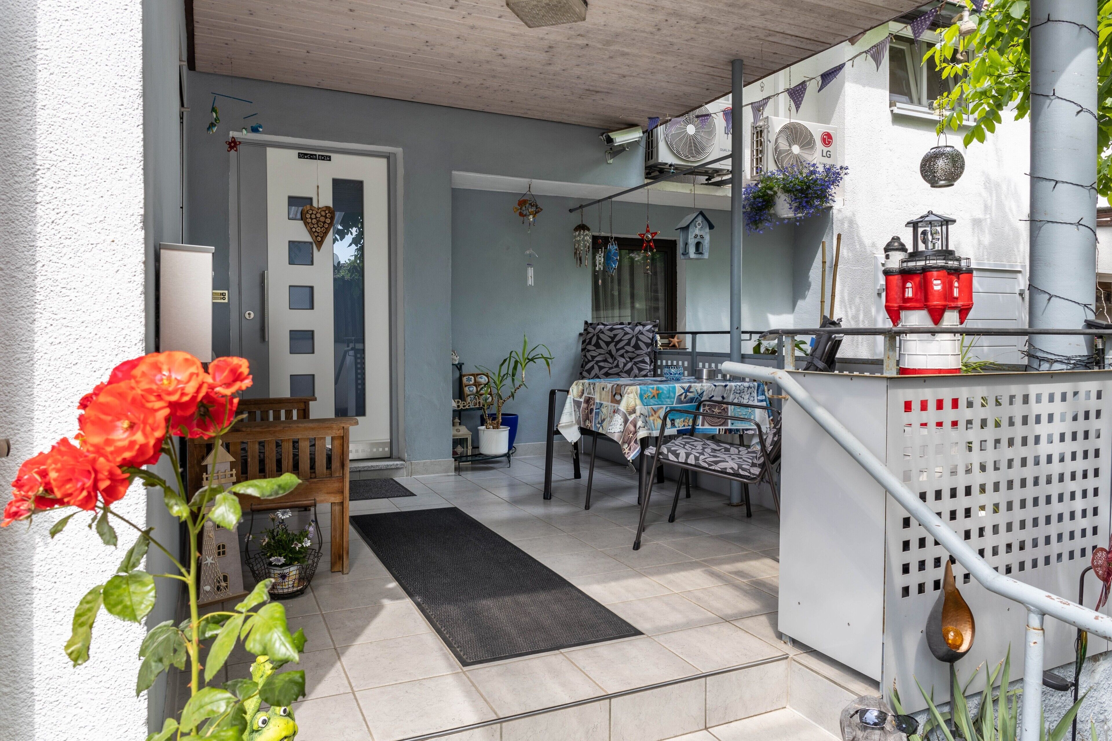 Ein Zimmer mit Esstisch, Stühlen, einer Bank, einem kleinen Gartenbereich mit Topfpflanze und einem Balkon mit Geländer.