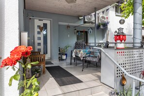 A room with a dining table, chairs, a bench, a small garden area with a potted plant, and a balcony with a railing.