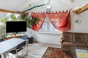 A living room with a TV, sofa, dining table, chairs, a red curtain, a clock, and a window with a view. - Apartment 'A Casa Alfred Kemmern - Neu' with Shared Terrace, Wi-Fi and Air Conditioning (Kemmern)