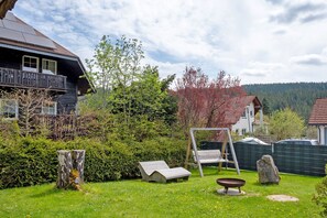 A residential property with a wooden deck, a swing set, a stone, and a metal chair.