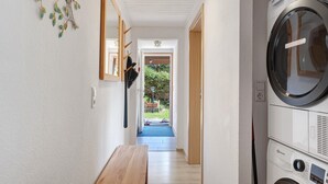 Un cuarto de lavandería con lavadora, un banco y una puerta que da a un jardín.