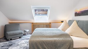 Une chambre de style loft moderne, avec un plafond en pente, une lucarne, un lit, un canapé et une petite table d’appoint.