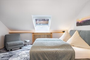 Une chambre de style loft moderne, avec un plafond en pente, une lucarne, un lit, un canapé et une petite table d’appoint.