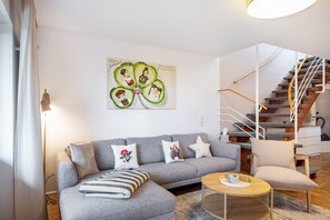 Una sala de estar moderna con un sofá gris, una mesa de centro redonda y una escalera con barandilla de madera.