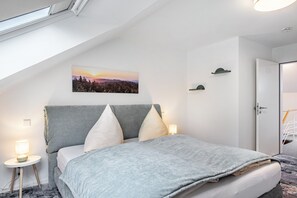 Un dormitorio con una cama, una mesita de noche, un estante en la pared y una puerta.